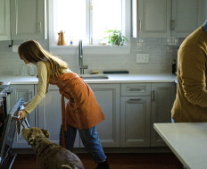 Two individuals and a dog in a well-lit kitchen