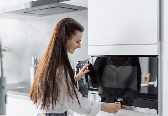 Smiling beautiful woman housewife preparing food in electric microwave oven