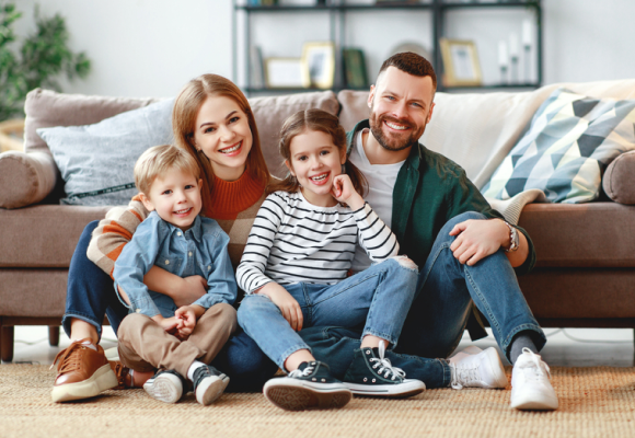 Happy family of four sitting together on the floor in their living room