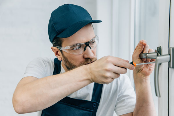 Locksmith in safety glasses repairing a door handle with a screwdriver